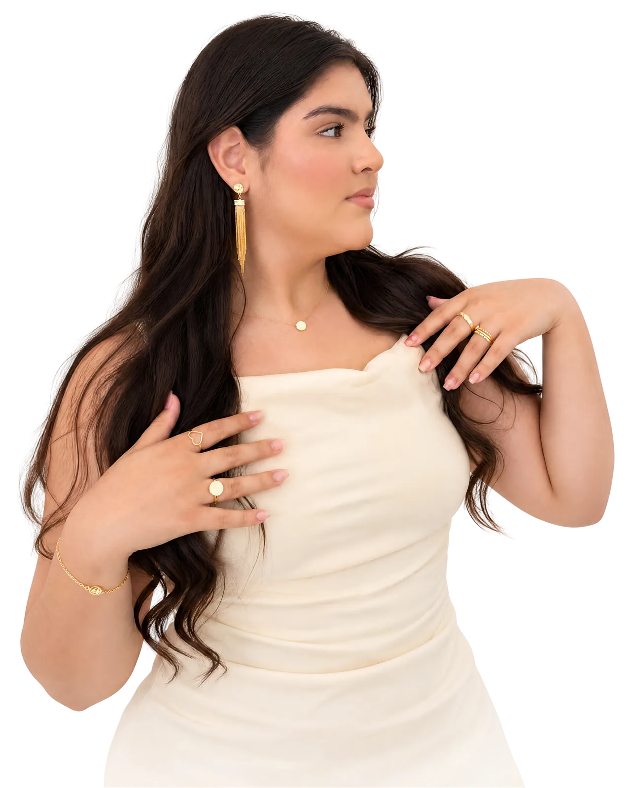 Mulher de pele morena clara e cabelo castanho-escuro longo e ondulado, de perfil, com brinco longo de franjas douradas, colar fino com pingente redondo, anéis dourados empilhados nas duas mãos e pulseira fina de corrente dourada.